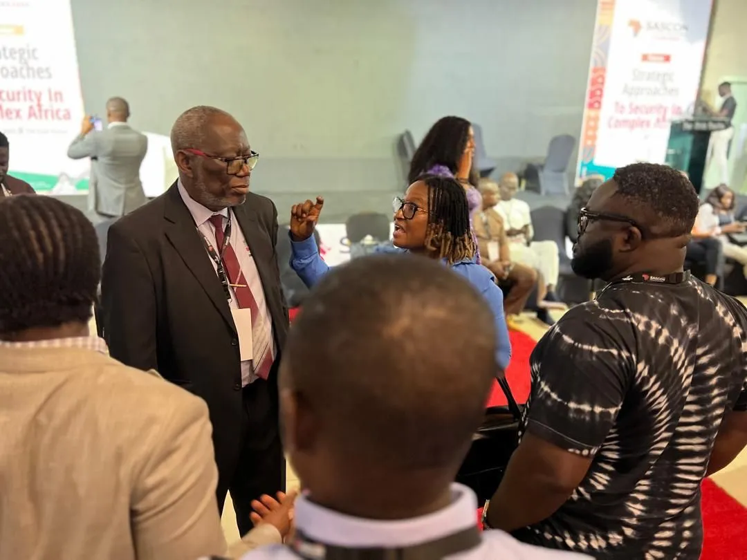 Delegates in conversation between sessions at SASCON, standing in a group with lanyards visible and conference banners behind them.