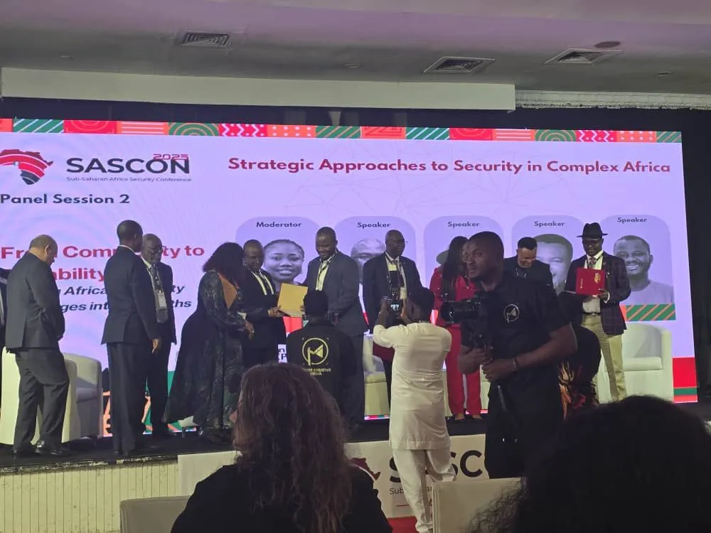 A panel session on the SASCON 2025 stage, with the moderator and speakers shown on the screen behind and a presentation being made to one of the panellists.