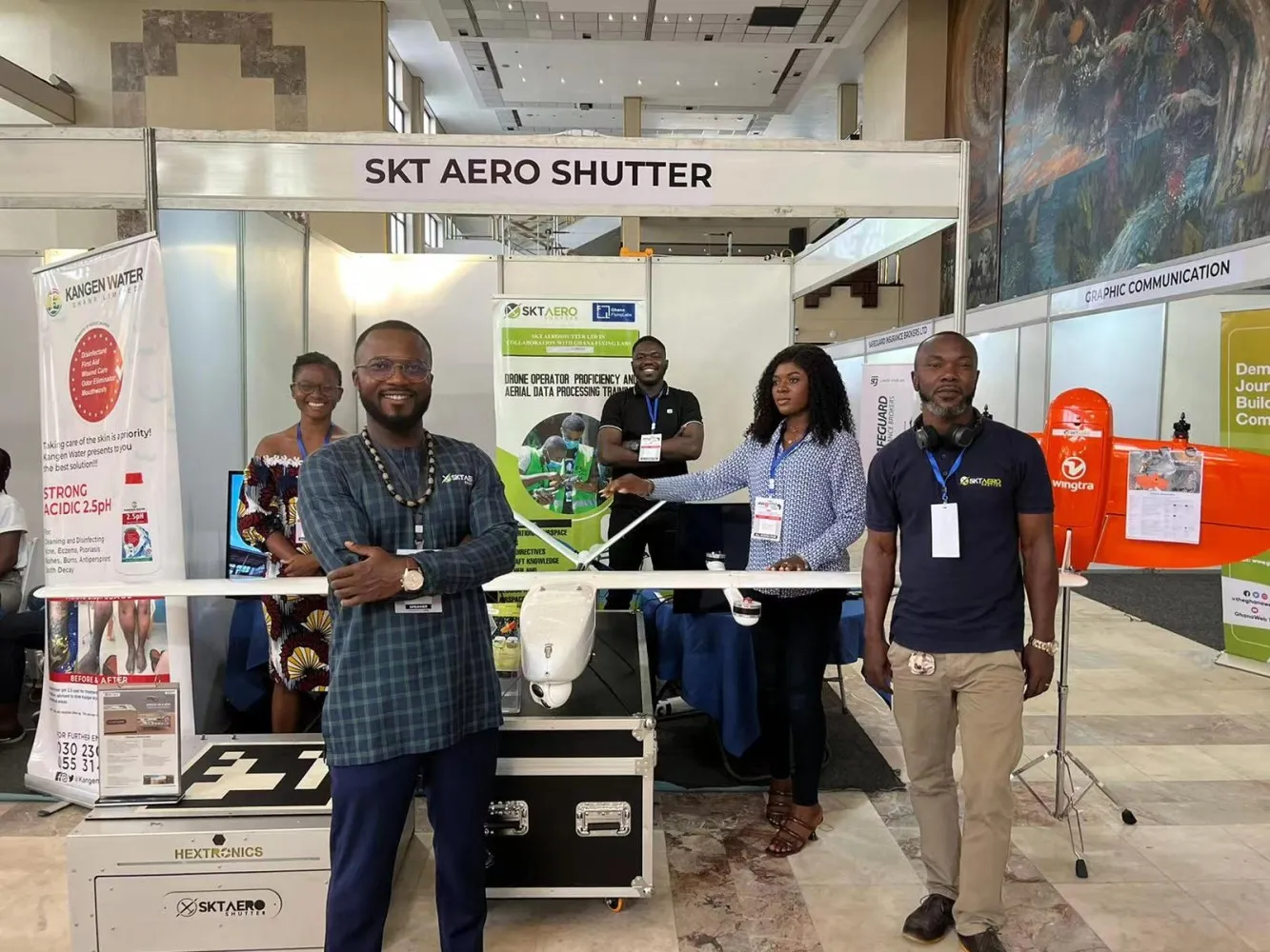 An exhibitor stand on the SASCON exhibition floor, with a fixed-wing survey drone displayed on the counter and five people standing at the stand.